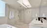 Bathroom featuring a skylight, walk-in glass-enclosed shower with stone tile surround, dual-sink vanity with light stone countertop, and deep soaking 