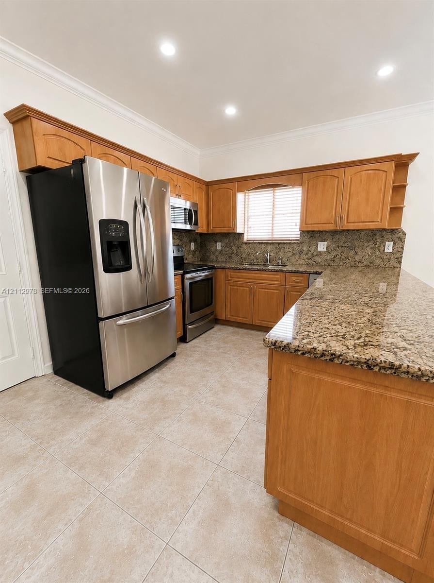Kitchen featuring wood cabinetry, stone countertops, stainless steel appliances, ceramic tile flooring, and recessed lighting