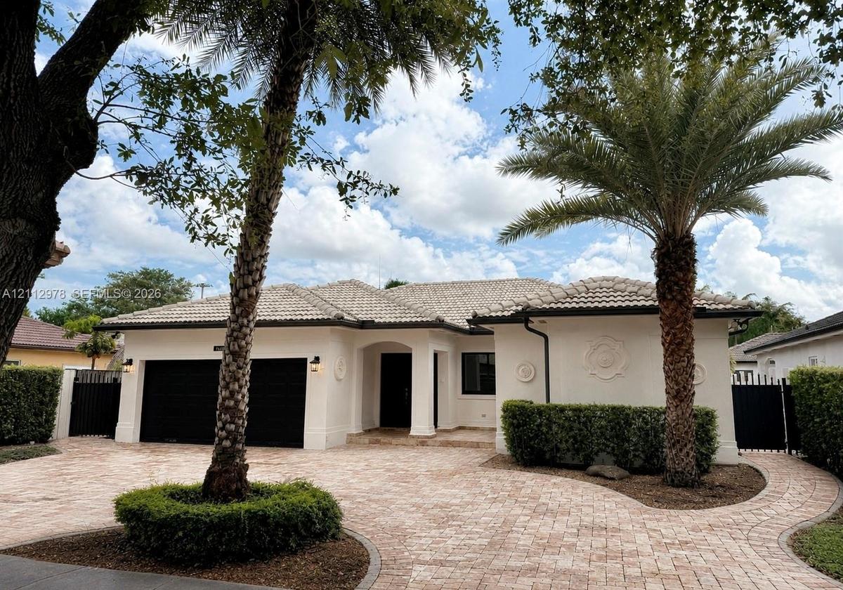 Stucco exterior featuring a tiled hip roof, custom masonry paver driveway, two-car garage with black doors, and ornamental wall medallions