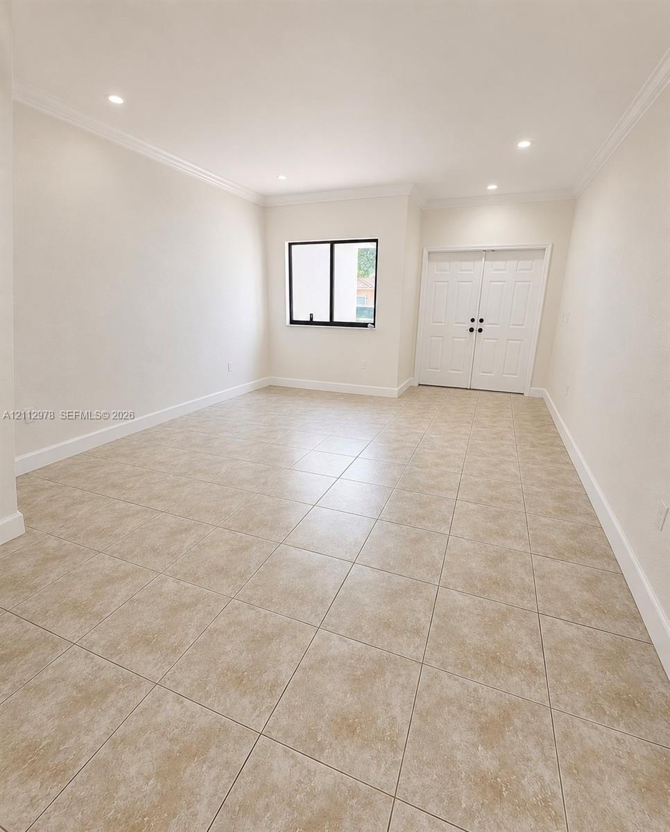 Neutral-toned ceramic tile flooring, recessed lighting, crown molding, double doors, and a single-pane window