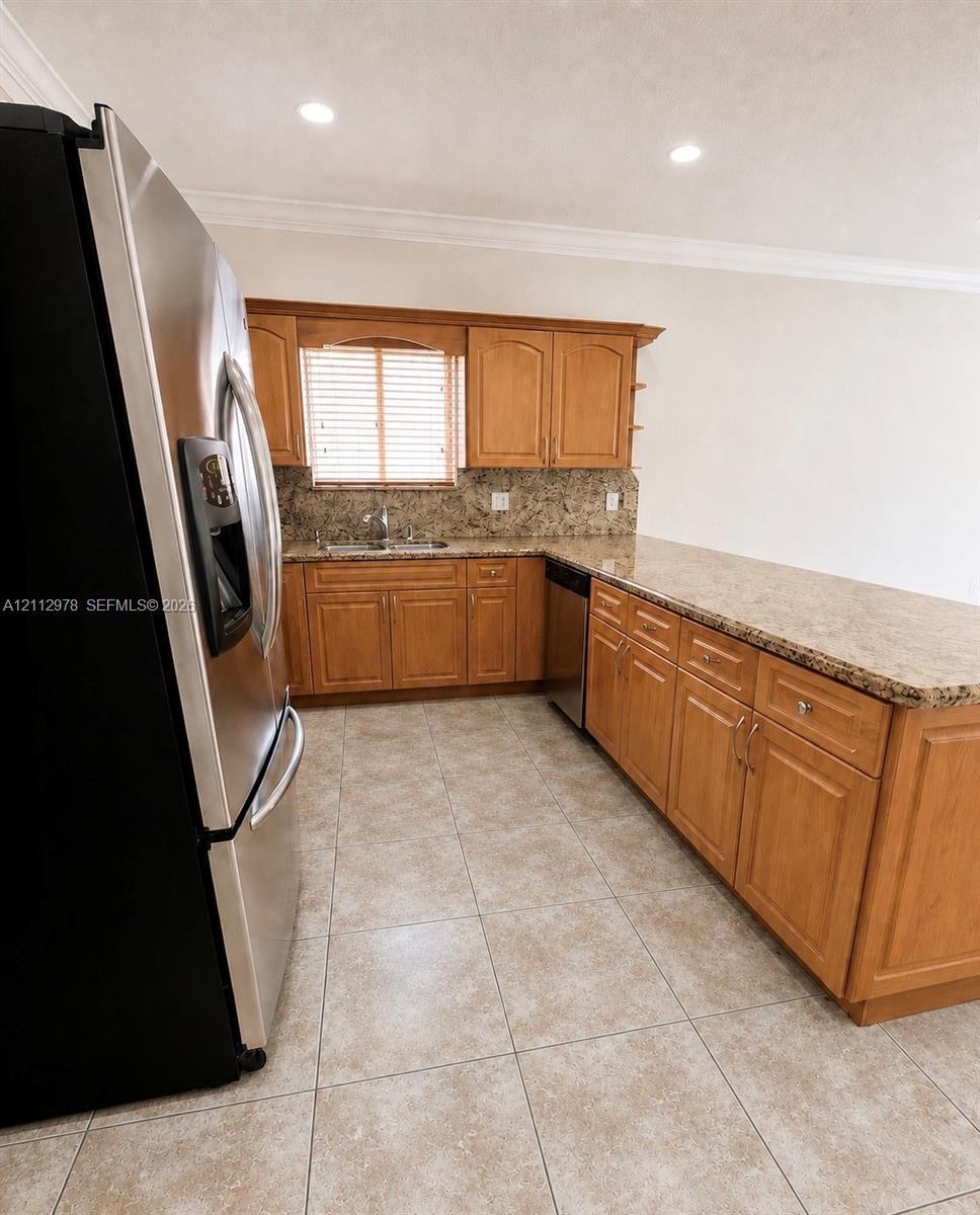 Kitchen featuring natural-finish wood cabinetry, stone-patterned countertops, stainless steel refrigerator, recessed lighting, and tile flooring