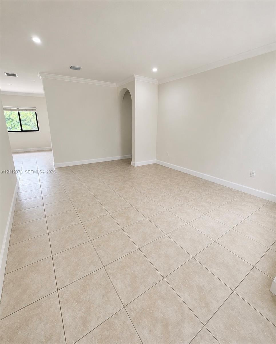 Neutral-toned tile flooring, recessed ceiling lighting, crown molding, and a distinctive arched architectural feature