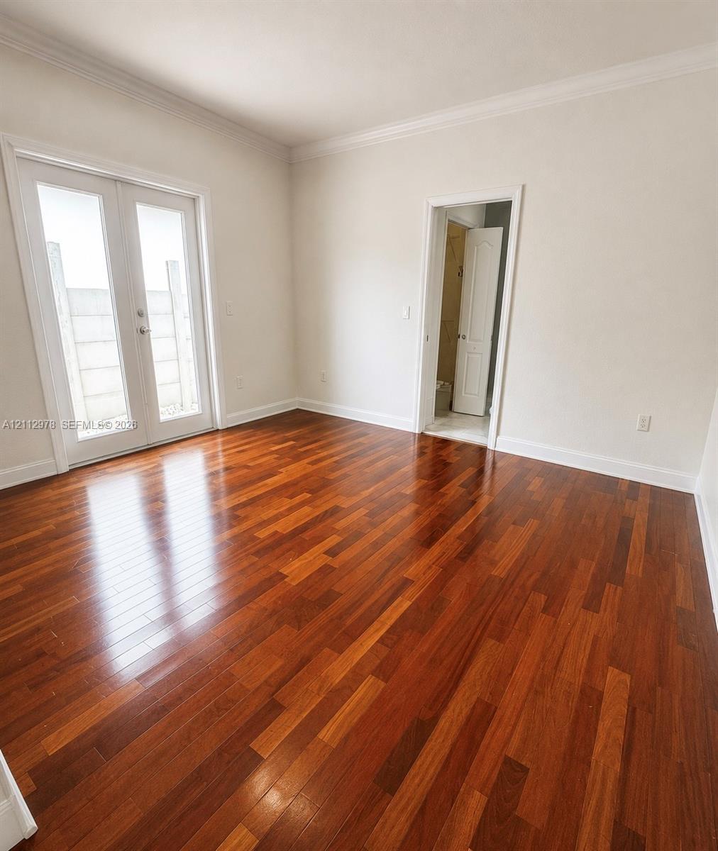 Room featuring wood-finish flooring, crown molding, and glass-paneled double doors