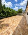 Outdoor patio area featuring herringbone-patterned stone pavers, privacy-focused mature hedge landscaping, and a perimeter concrete block wall