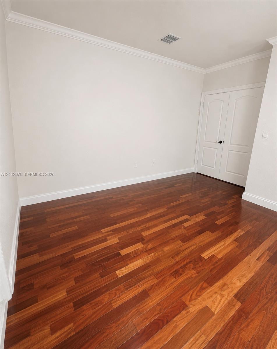 Room featuring wood-finish flooring, neutral wall paint, crown molding, and double-panel doors with matte black hardware
