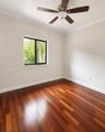 Wood-finish flooring, neutral wall color, single-pane window with black frame, and a multi-blade ceiling fan with central light fixture