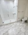 Walk-in shower featuring white subway tile surround, frameless glass door, and integrated shelving, complemented by stone-patterned floor tile and a d