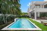 Rear exterior featuring a rectangular pool with a built-in water feature, natural stone coping, covered patio, outdoor kitchen, and synthetic turf law