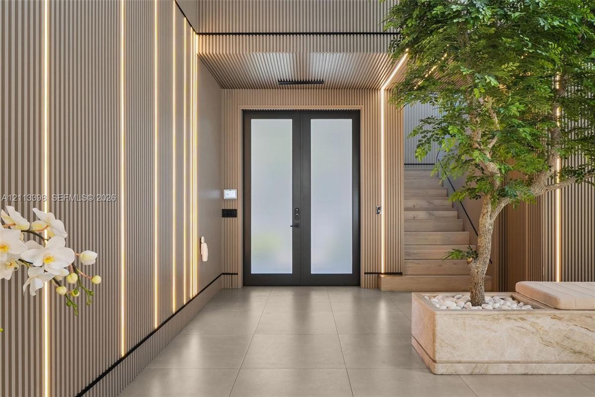 Entryway featuring vertical wood-slat wall paneling, integrated linear lighting, large-format tile flooring, double doors with frosted glass, and a bu