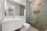 Modern wall-mounted vanity with integrated sink, full-width mirror, walk-in shower with floor-to-ceiling stone-finish tile, glass shower enclosure, an