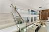 Open-concept interior featuring stone-finish flooring, a glass and metal staircase railing, a multi-level wood-panel wall feature, a stone-topped kitc