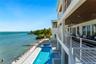 Multi-level waterfront residence featuring a lap pool with an integrated spa, expansive covered balcony with slatted wood-finish ceilings, metal raili