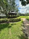 Outdoor gazebo featuring a tiered roof and dark wood structure, situated among mature landscaping with a paved walkway