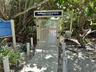 Secured entry gate with access control system, elevated walkway, and roped pathway markers surrounded by mature native landscaping