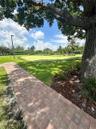 Expansive grounds featuring a manicured putting green, brick paver walkway, mature tree canopy, and landscape lighting