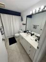 Bathroom featuring a vanity with a white countertop and oval undermount sink, large wall-mounted mirror, multi-bulb light fixture, and stone-finish fl