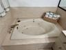 Drop-in soaking tub with integrated water jets, stone-tiled surround, and metallic finish faucet hardware
