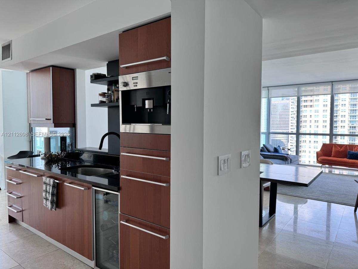 Kitchen featuring wood-veneer cabinetry, integrated coffee station, dark stone countertops, under-counter wine refrigerator, and polished stone floori