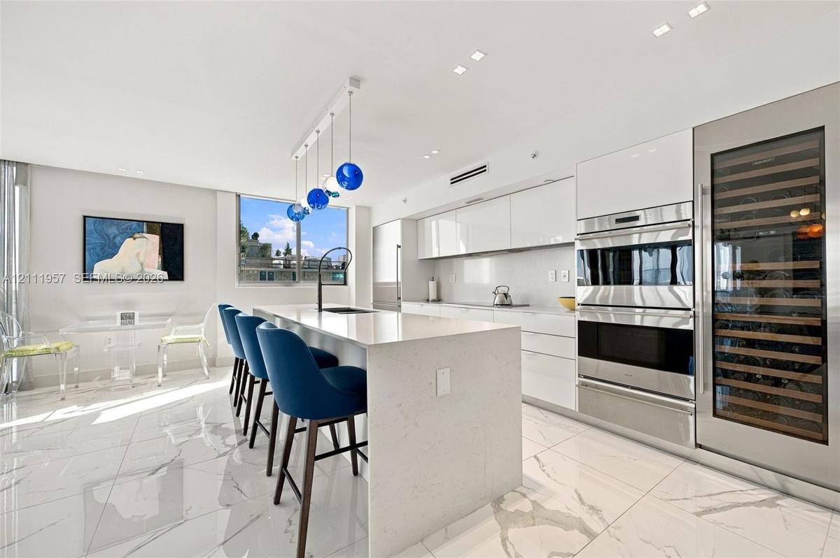 Kitchen featuring high-gloss cabinetry, a waterfall-edge island with a quartz countertop, stone-finish flooring, built-in stainless steel appliances, 