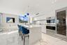 Kitchen featuring high-gloss cabinetry, a waterfall-edge island with a quartz countertop, stone-finish flooring, built-in stainless steel appliances, 