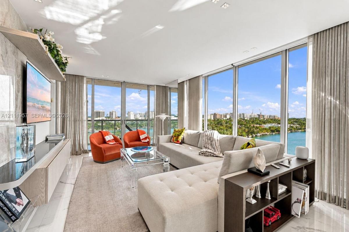 Floor-to-ceiling glass windows, stone-finish flooring, and a wall-mounted light-wood cabinetry unit