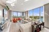 Floor-to-ceiling glass windows, stone-finish flooring, and a wall-mounted light-wood cabinetry unit