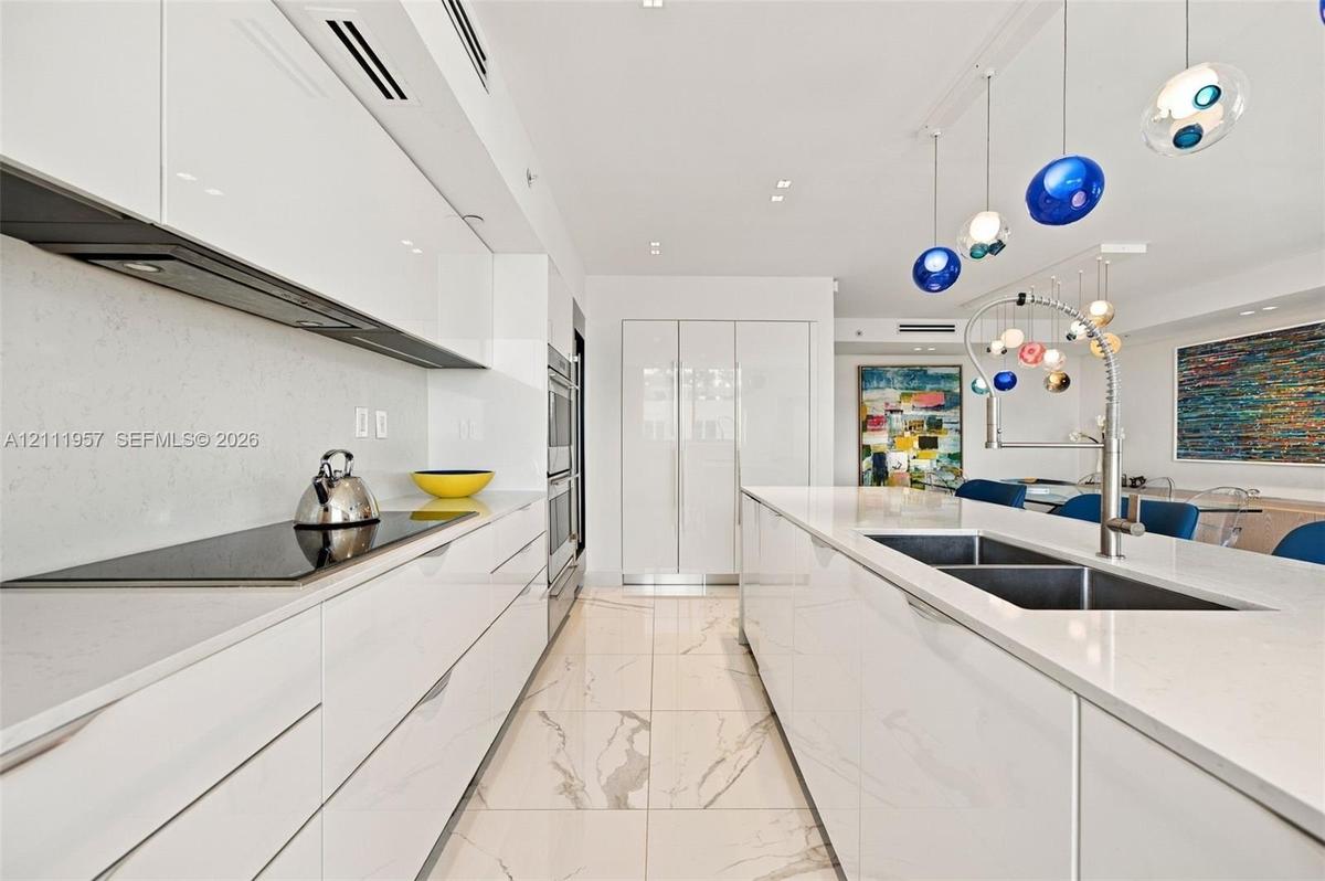 Contemporary kitchen featuring high-gloss cabinetry, quartz countertops, large-format veined tile flooring, a stainless steel double-basin sink with p