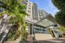 Multi-story residential building exterior featuring a glass-canopy entryway, tiered balconies with glass railings, vertical gardens, and stone-tiled f