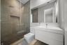 Walk-in shower with floor-to-ceiling tile, rainfall showerhead, and glass enclosure, featuring a white floating vanity with an integrated basin and a 