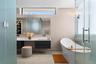 Floating dual-vanity with matte cabinetry and solid-surface countertop, freestanding soaking tub, frameless glass-enclosed shower, clerestory window, 
