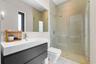 Wall-mounted dark cabinetry with a white rectangular sink basin, large frameless wall mirror, walk-in glass-enclosed shower, and neutral-toned wall ti