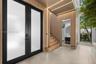 Double-entry door with frosted glass panels, wood-slat wall paneling with integrated LED lighting, large-format tile flooring, and a floating staircas