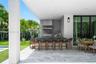 Covered outdoor patio featuring light-toned stone tile flooring, a built-in outdoor kitchen with a stainless steel range hood, natural stone backsplas