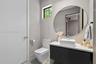 Floating dark-finish vanity with a white rectangular vessel sink, solid-surface countertop, circular frameless mirror, and dual-flush toilet