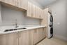 Laundry room featuring light wood-finish cabinetry, white solid-surface countertops, an undermount stainless steel sink with a high-arch pull-down fau