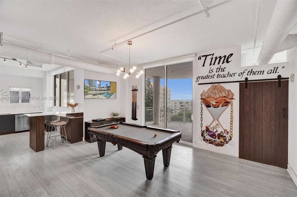Open-concept living space featuring wood-finish flooring, exposed overhead industrial piping, a multi-globe chandelier, and a wood-panel sliding barn 