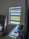 Single-pane window with a black frame, featuring retractable dual-layer blinds and water-fronting exterior exposure