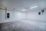 Finished garage featuring smooth walls, concrete flooring, dual overhead LED lighting fixtures, and an attic access panel