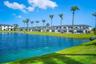 Waterfront exterior featuring a manicured lawn, established palm trees, and multi-unit residential structures with attached garages