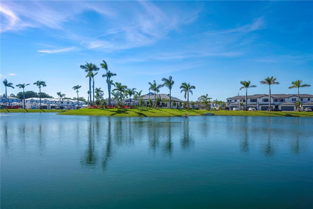 Waterfront property featuring a serene lake, manicured landscaping, and mature palm trees