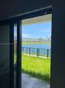 Black-framed sliding glass door opening to a paved patio, metal perimeter fencing, and waterfront scenery