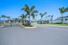 Gated community entrance featuring metal perimeter fencing, paved roadway, manicured landscaping, and mature palm trees