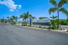 Gated community entrance featuring a masonry monument sign, asphalt paved roadway, and tropical landscaping