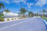 Community entrance featuring a branded masonry monument sign, mature palm landscaping, paved roadways, and gated access