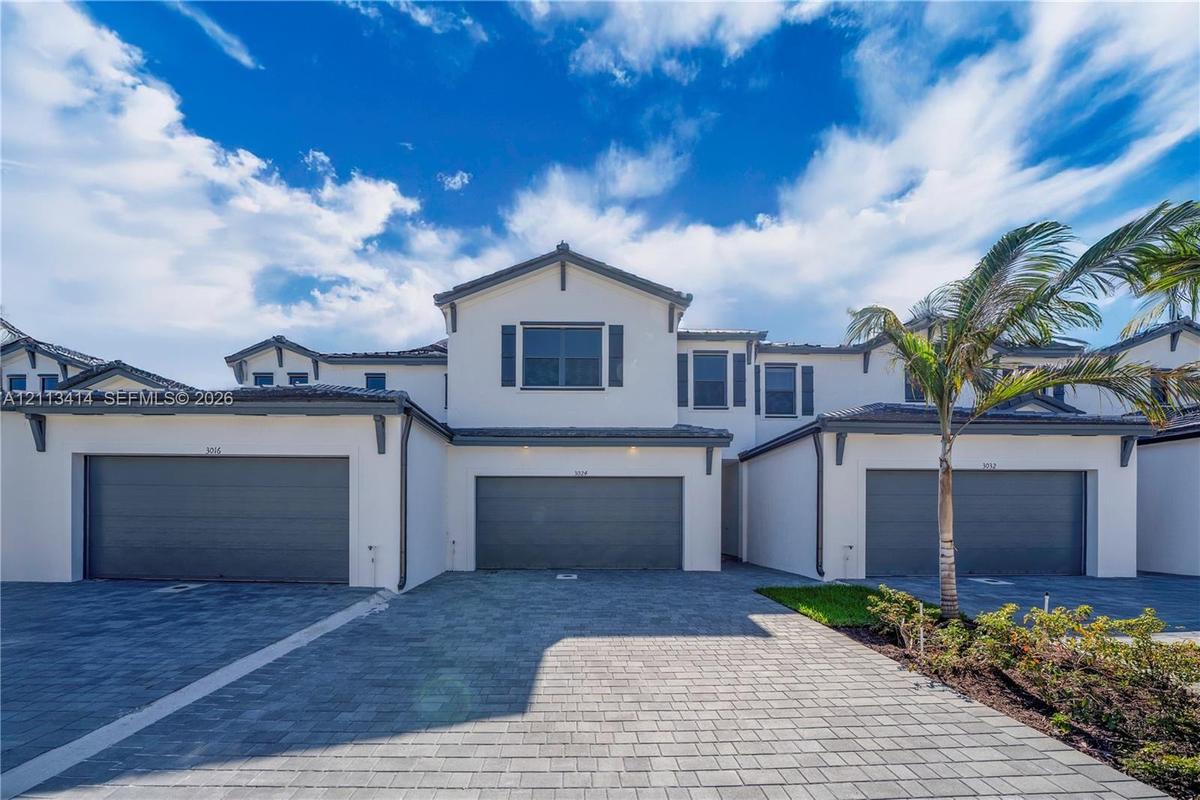 Multi-level stucco exterior featuring a tiled roof, grey-toned garage doors, and paver driveway