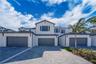 Multi-level stucco exterior featuring a tiled roof, grey-toned garage doors, and paver driveway