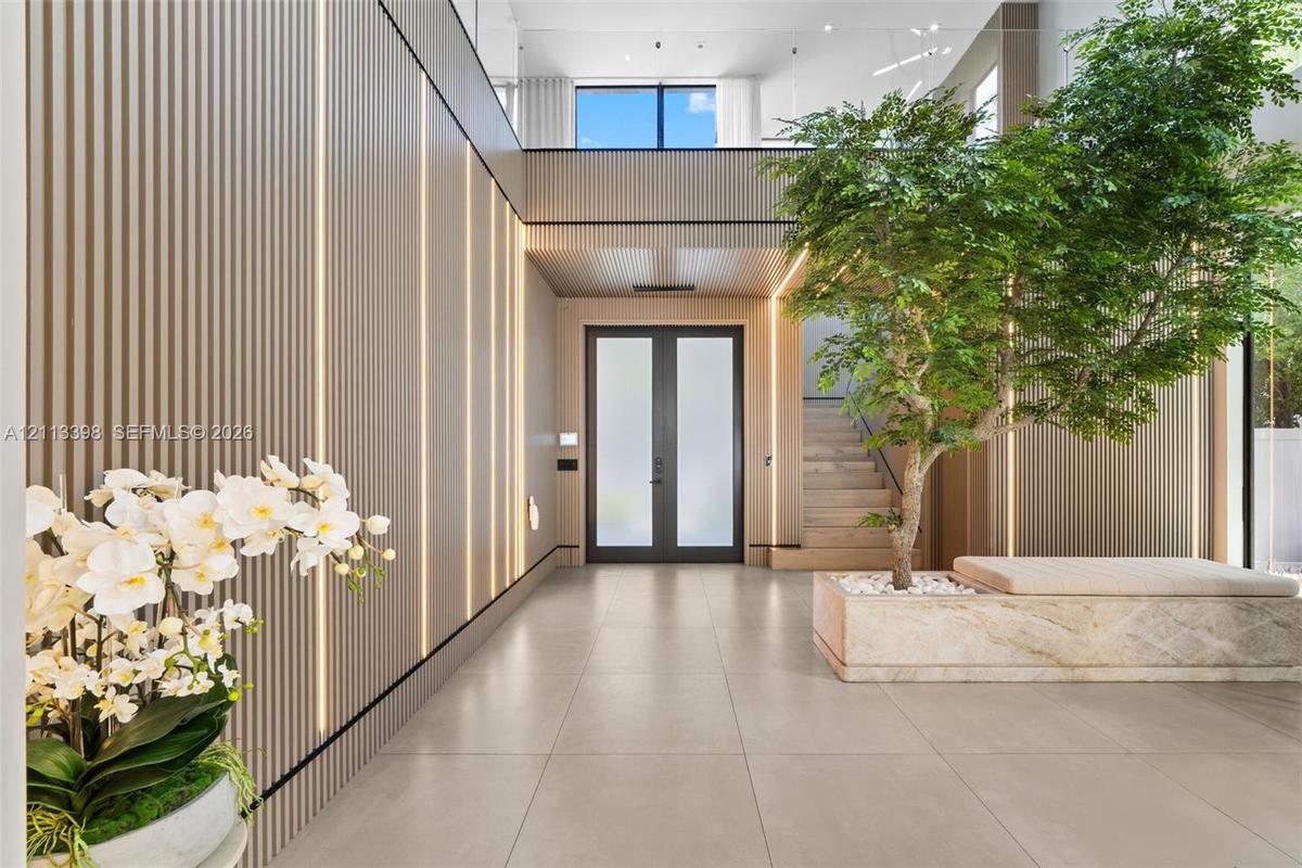 Double-height foyer featuring vertical slat wall paneling with integrated recessed lighting, large-format tile flooring, a glass-railed staircase, and