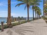Waterfront walkway featuring paved stone surfacing, mature palm trees, integrated landscape lighting, and a timber guardrail