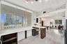 Expansive floor-to-ceiling windows, white-toned wood-finish flooring, industrial-style exposed ductwork, and built-in breakfast bar featuring a sleek 