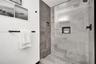 Walk-in shower featuring large-format grey tile surround, pebble-texture floor, frameless glass enclosure, built-in recessed wall niche, and matte bla